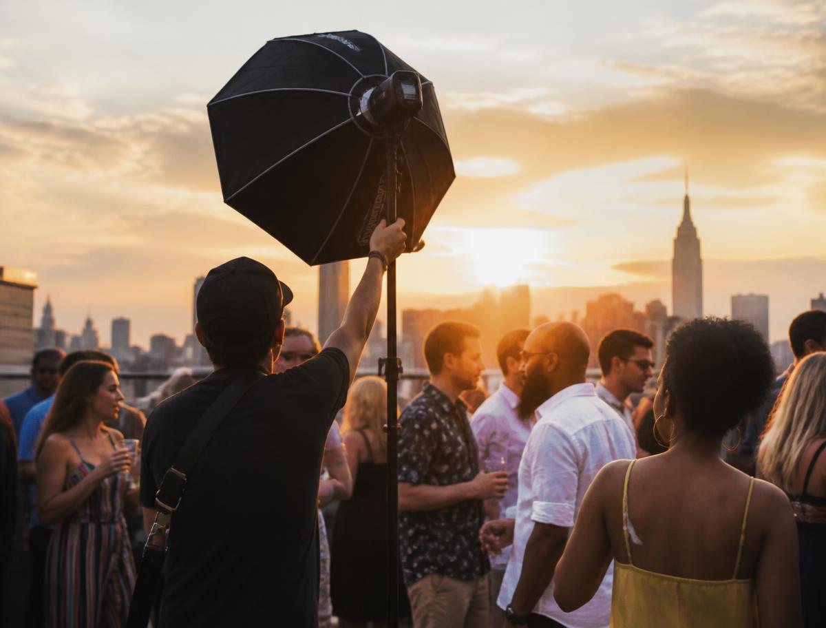 A photographer setting up lighting at a rooftop party at sunset
